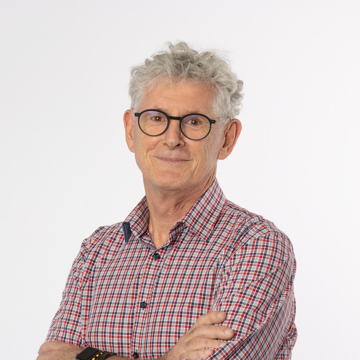 Greg in a red and blue checkered shirt standing with his arms folded.