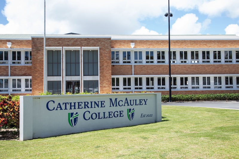 School sign in the grass in front of the main school building.